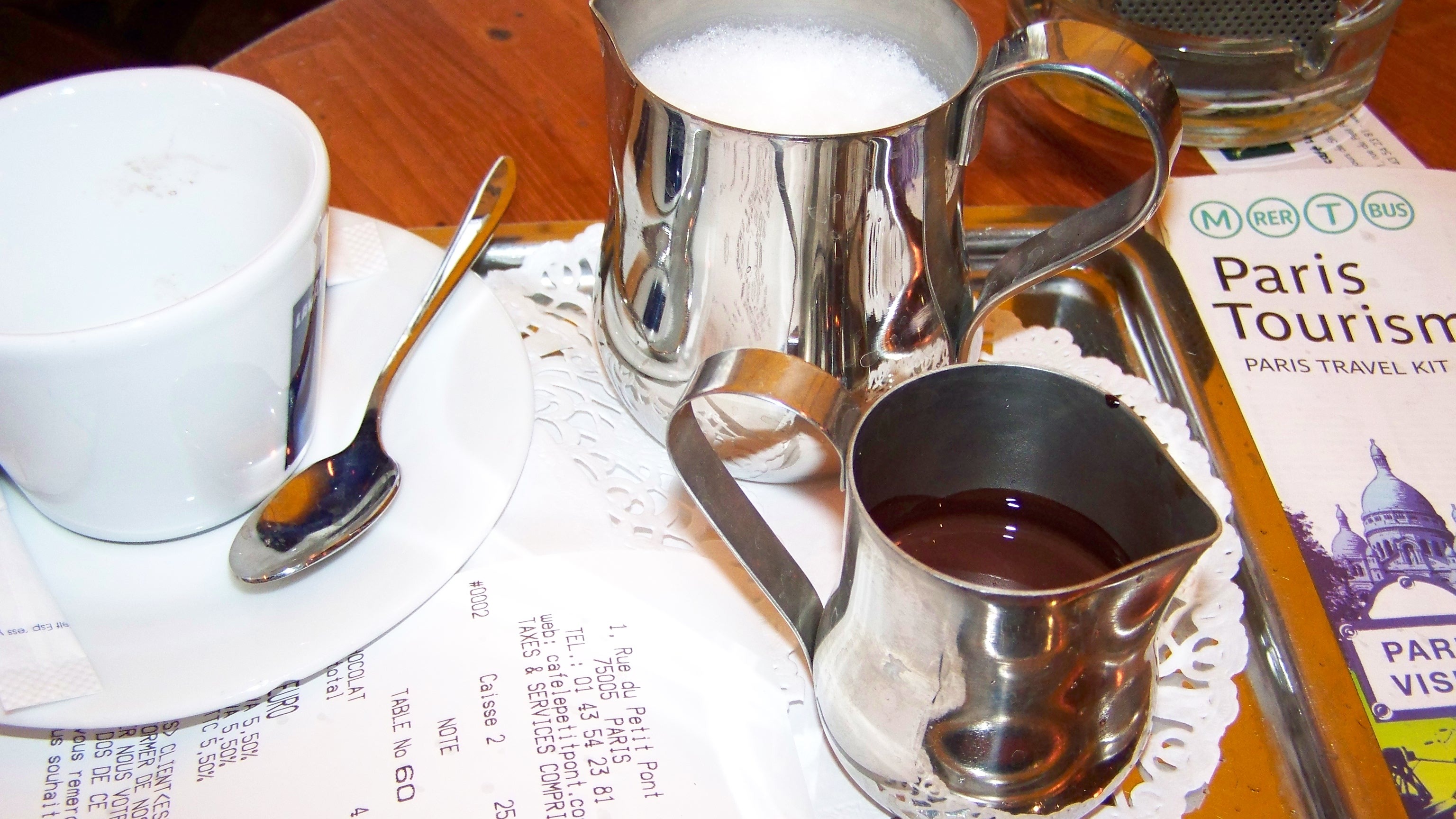 Hot chocolate service with silver pitchers, Paris bill and Paris Tourism guide on a cafe table